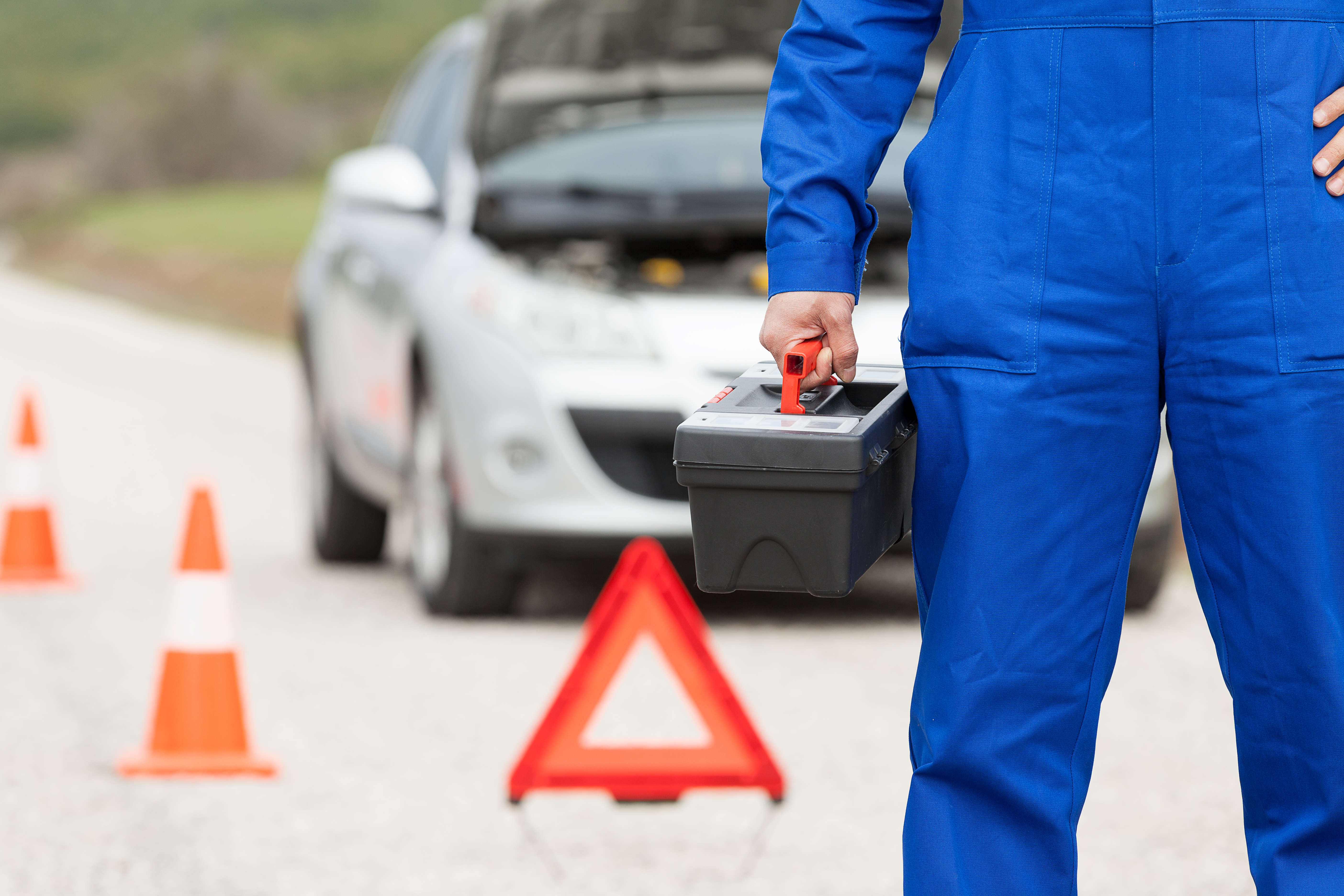 Auto mechanic with toolbox on road and damaged car on background.